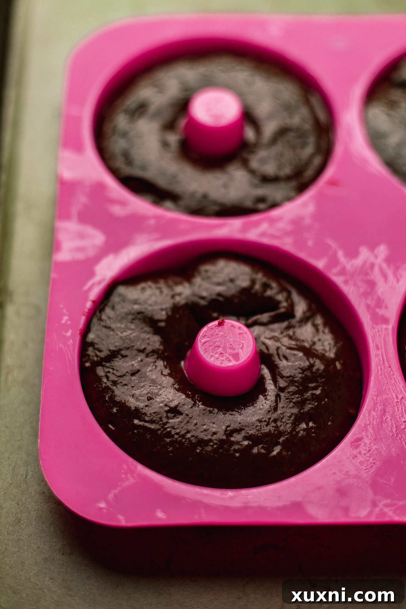 Piping vegan chocolate donut batter into a donut pan for baking.