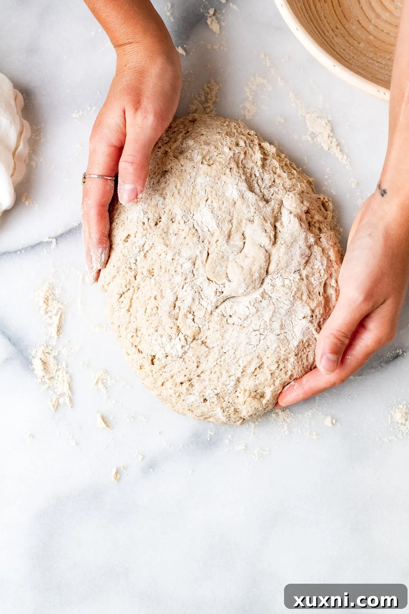 Hands gently kneading the gluten-free dough on a sorghum-floured surface after its first proof.