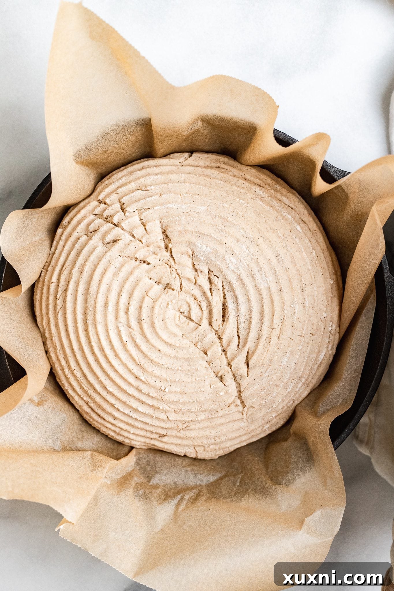 Scored gluten-free vegan bread dough on parchment paper, ready to be transferred to the hot cast iron skillet for baking.