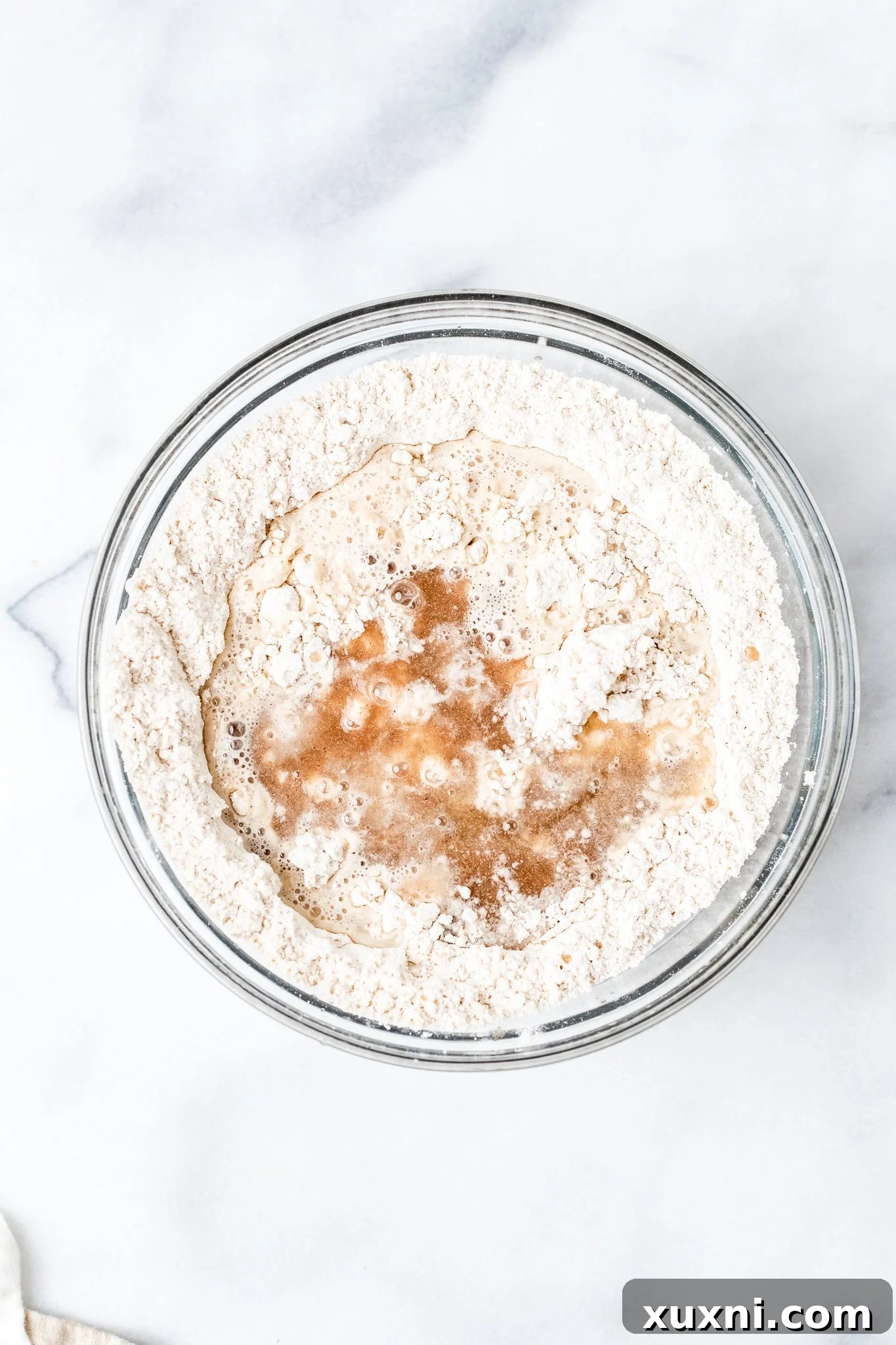 Hand adding psyllium husk gel and bloomed yeast mixture to dry gluten-free flours in a mixing bowl.