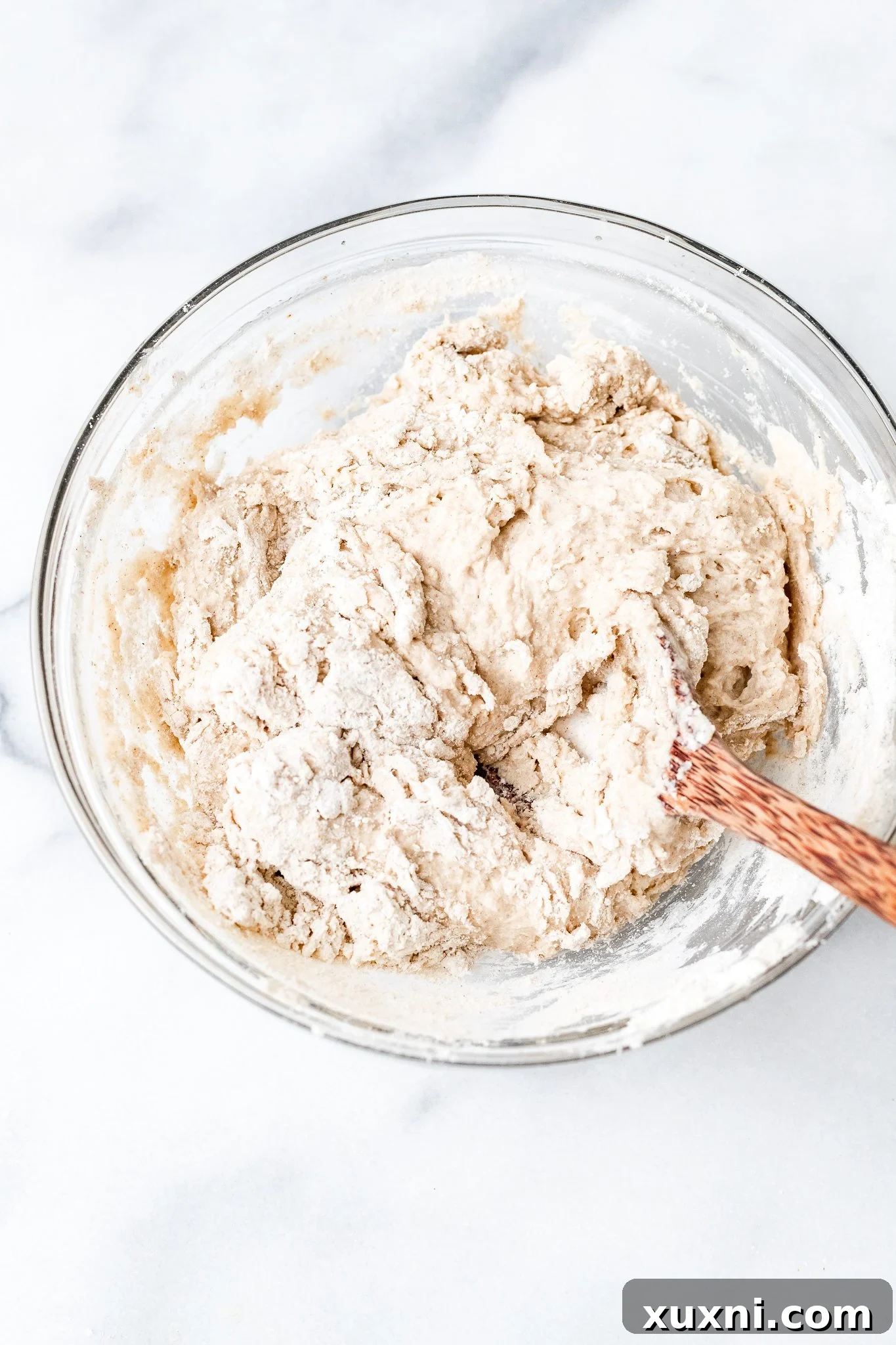 Close-up of gluten-free dough being mixed in a bowl with a wooden spoon, showing its developing texture.