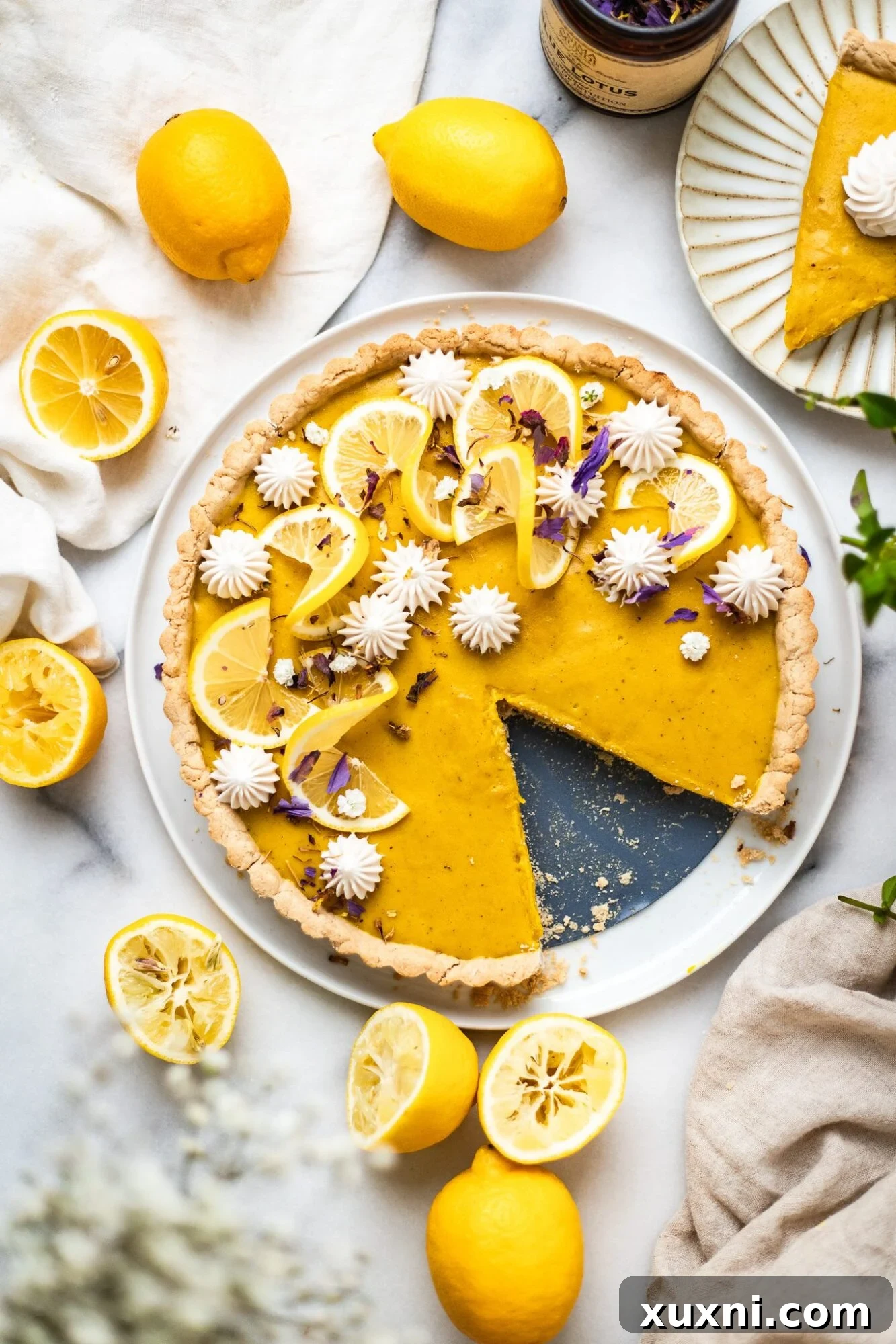 Easy vegan lemon tart on marble surface with fresh lemons and a spring-like setting, showcasing its vibrant yellow color and perfect crust.