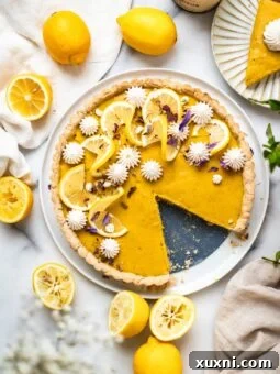Easy vegan lemon tart on marble surface with fresh lemons and a spring-like setting, showcasing its vibrant yellow color and perfect crust.