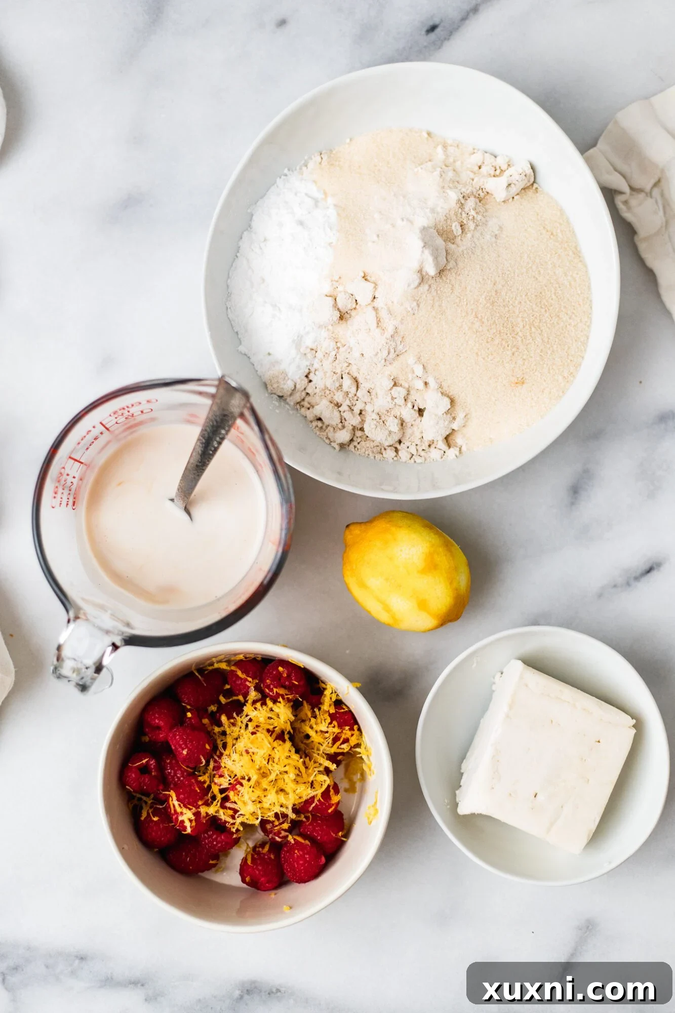 Selection of vegan scone ingredients including oat flour, butter, raspberries, and lemon.