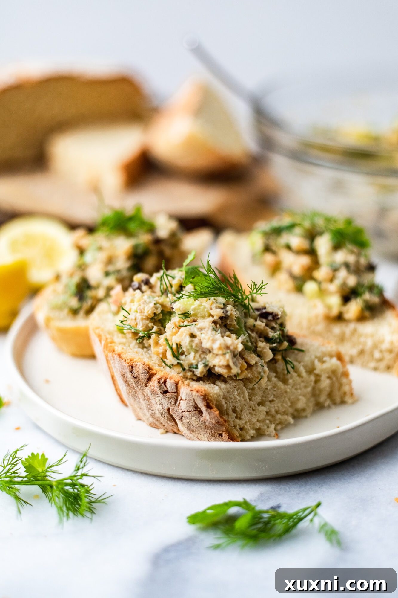 Plant Based Chickpea Tuna Salad 3 White plate showcasing slices of bread generously topped with homemade chickpea tuna salad and fresh parsley.