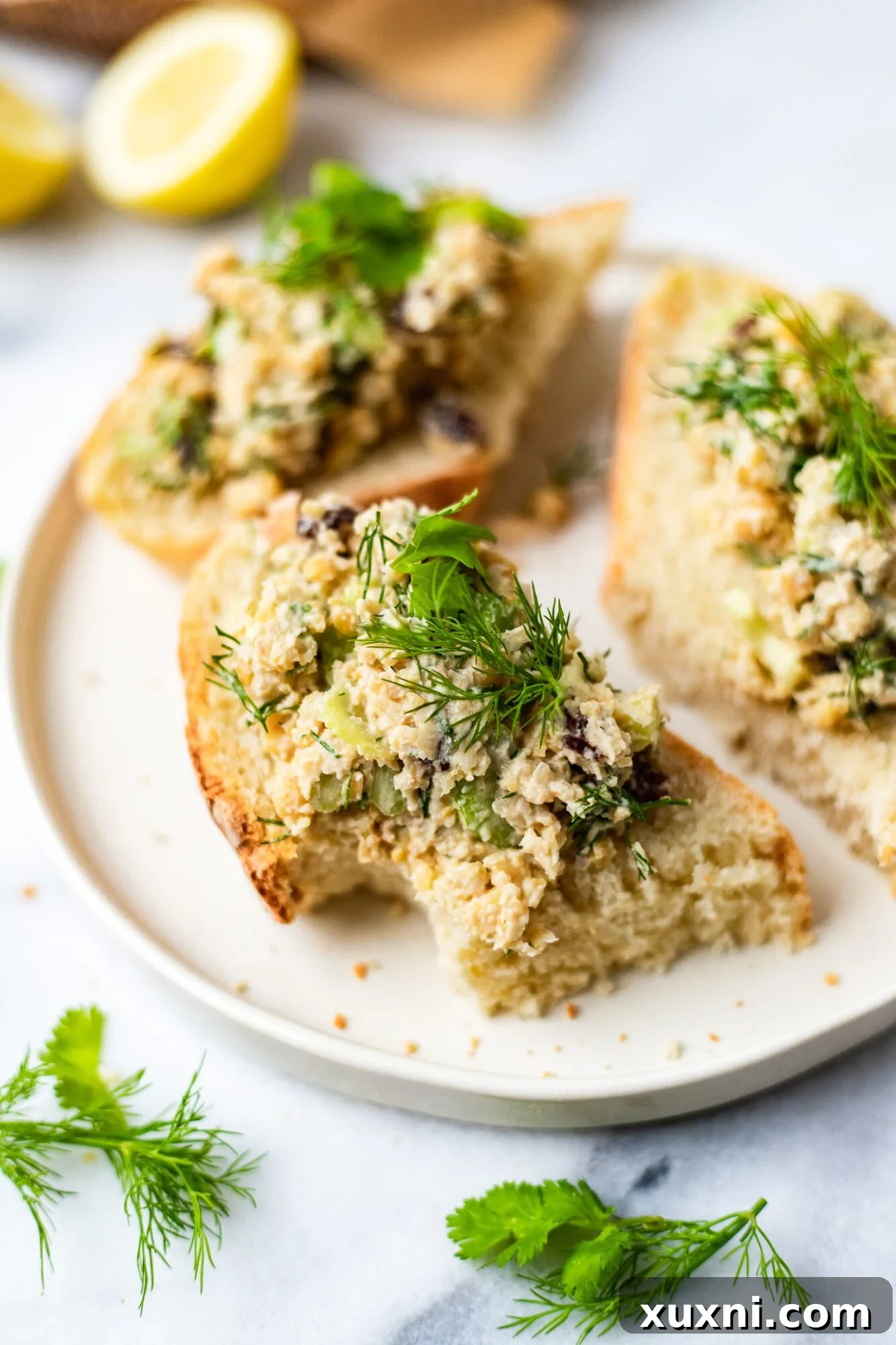 Plant Based Chickpea Tuna Salad 8 A slice of bread with vegan tuna salad, showing a bite taken, placed on a clean white plate.
