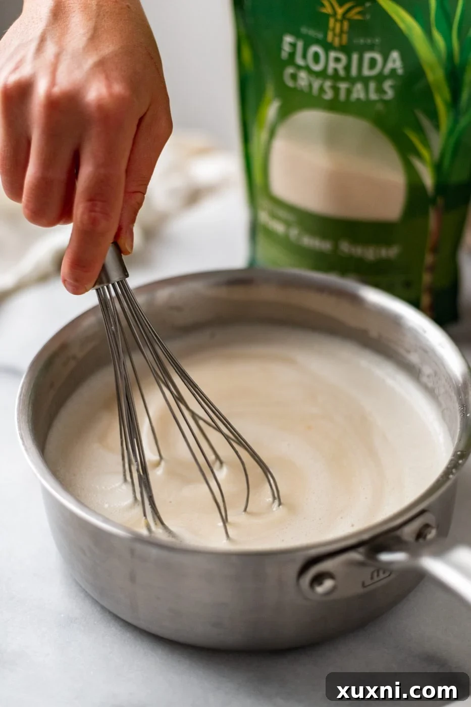 A spoon stirring the coconut cream mixture in a saucepan, demonstrating its thickening process on low heat.