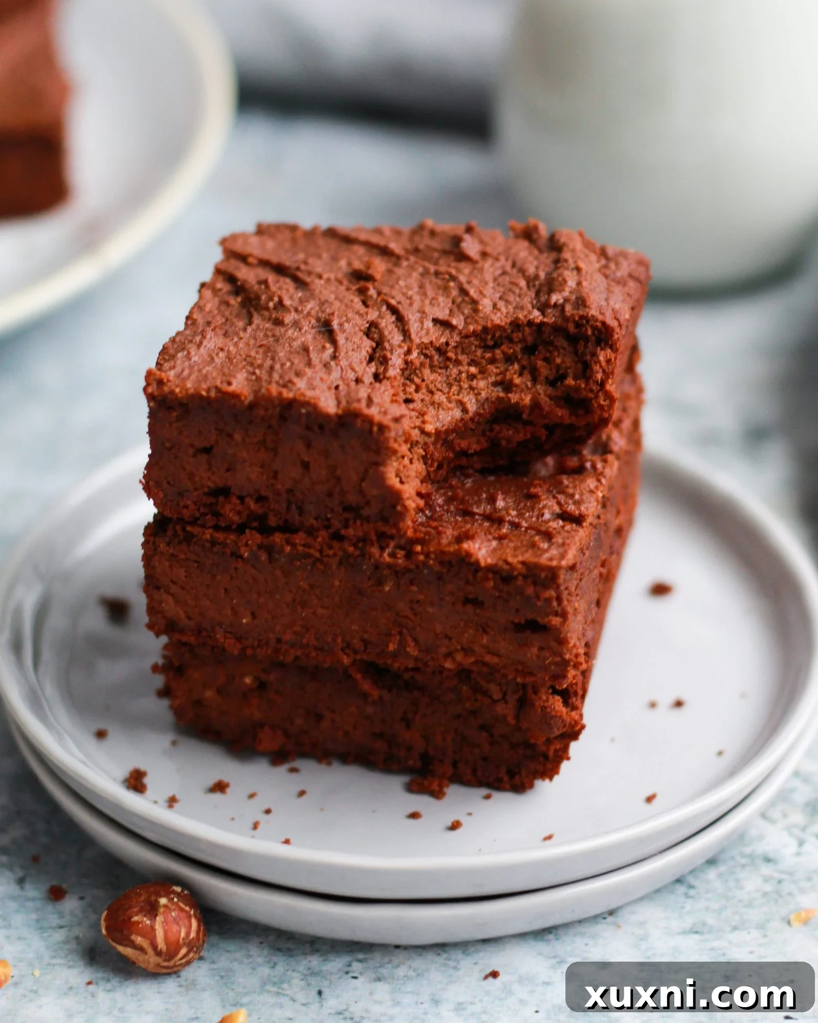 A stack of healthy vegan Nutella brownies with a bite taken out of the top one, revealing its dense, moist interior.