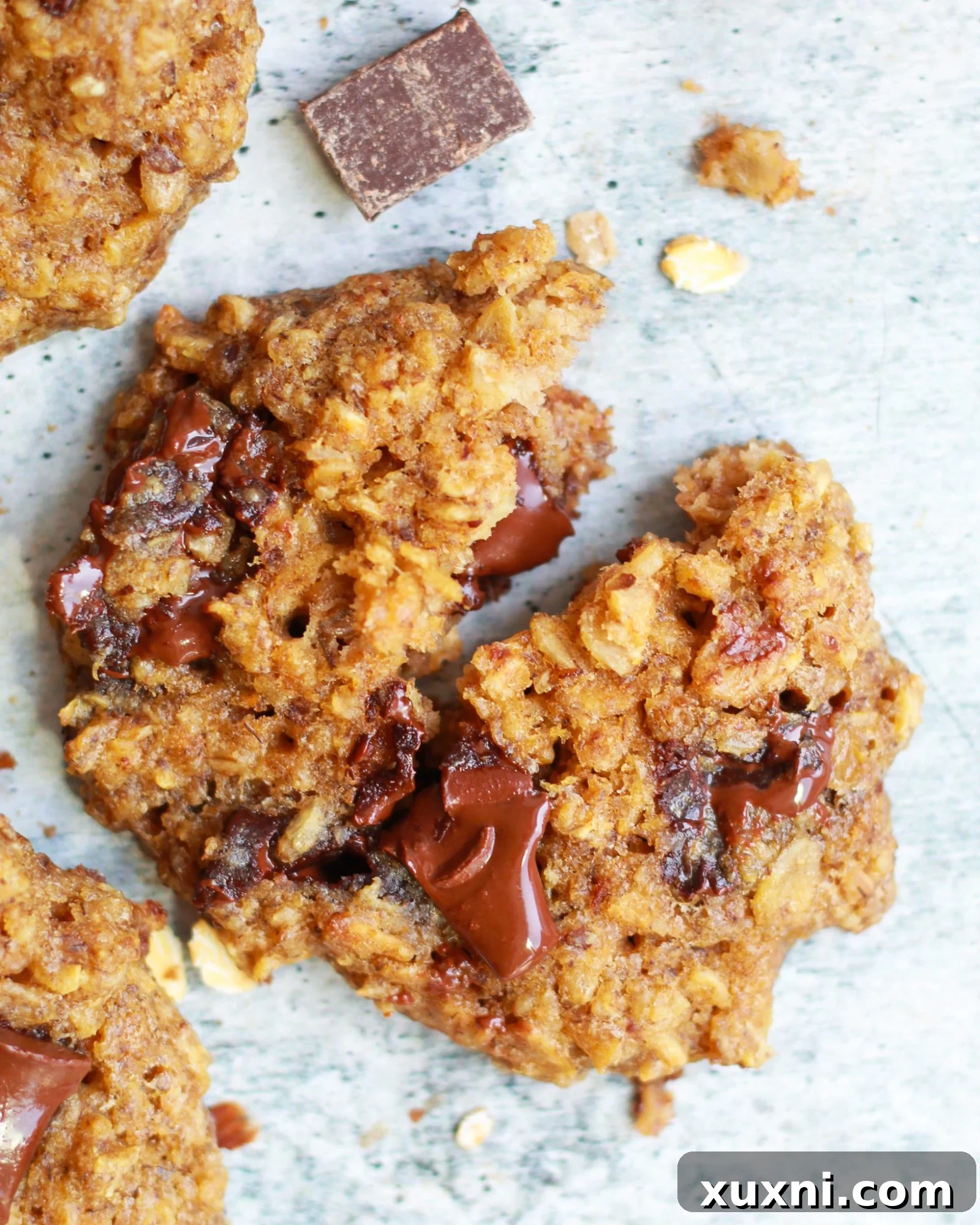 Large, broken in half, healthy vegan oatmeal chocolate chip cookie showing its chewy texture and melty chocolate chips.