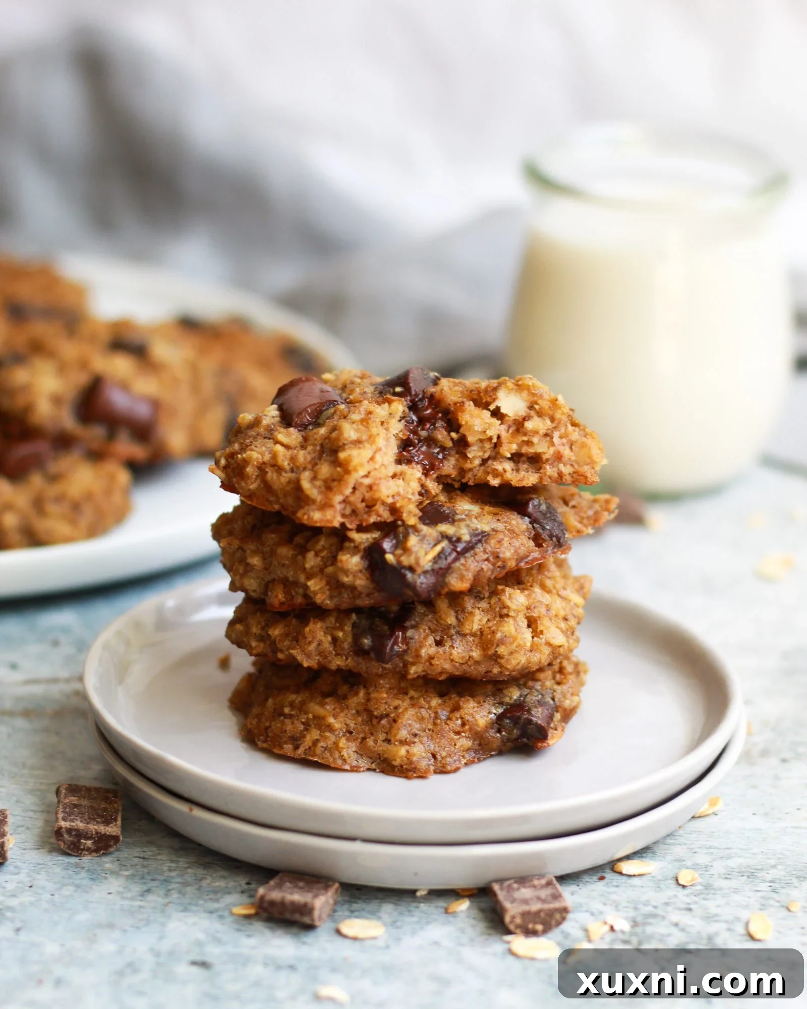 A stack of four perfectly baked healthy vegan oatmeal chocolate chip cookies, showcasing their golden-brown edges and soft centers.