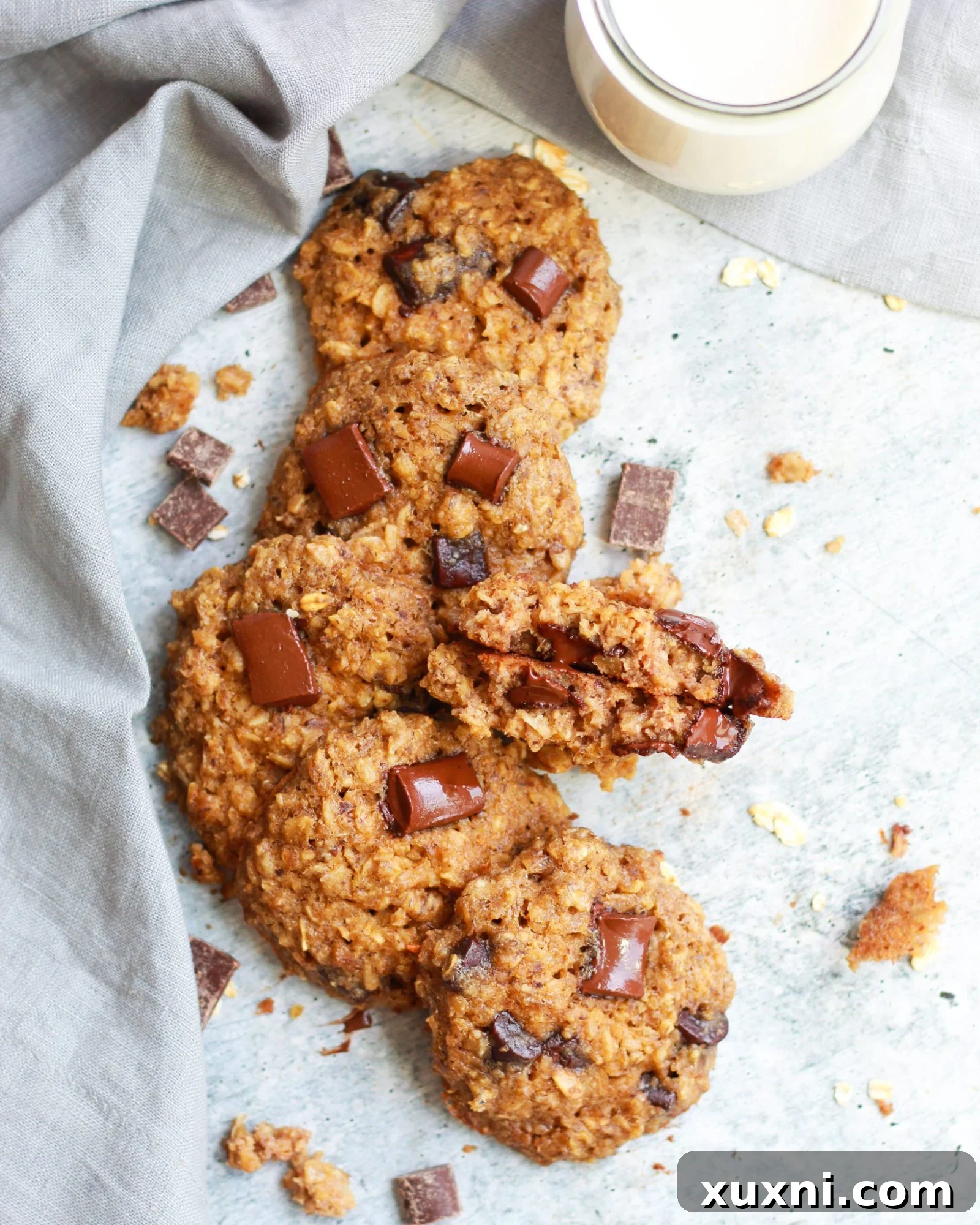 A line of healthy vegan oatmeal chocolate chip cookies on a baking sheet, with one cookie broken to show its soft interior.