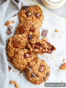 Five healthy vegan oatmeal chocolate chip cookies with a sixth broken in half, beside a glass of almond milk.