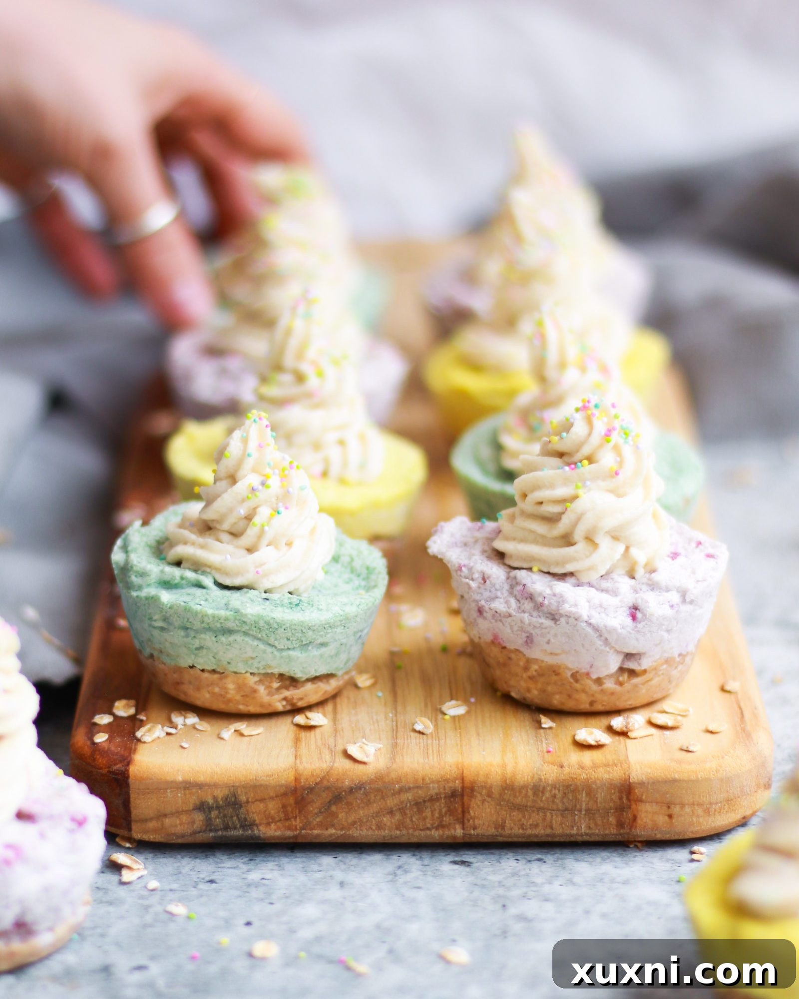 A hand reaching for a mini vegan cheesecake from a display of several colorful cheesecakes.