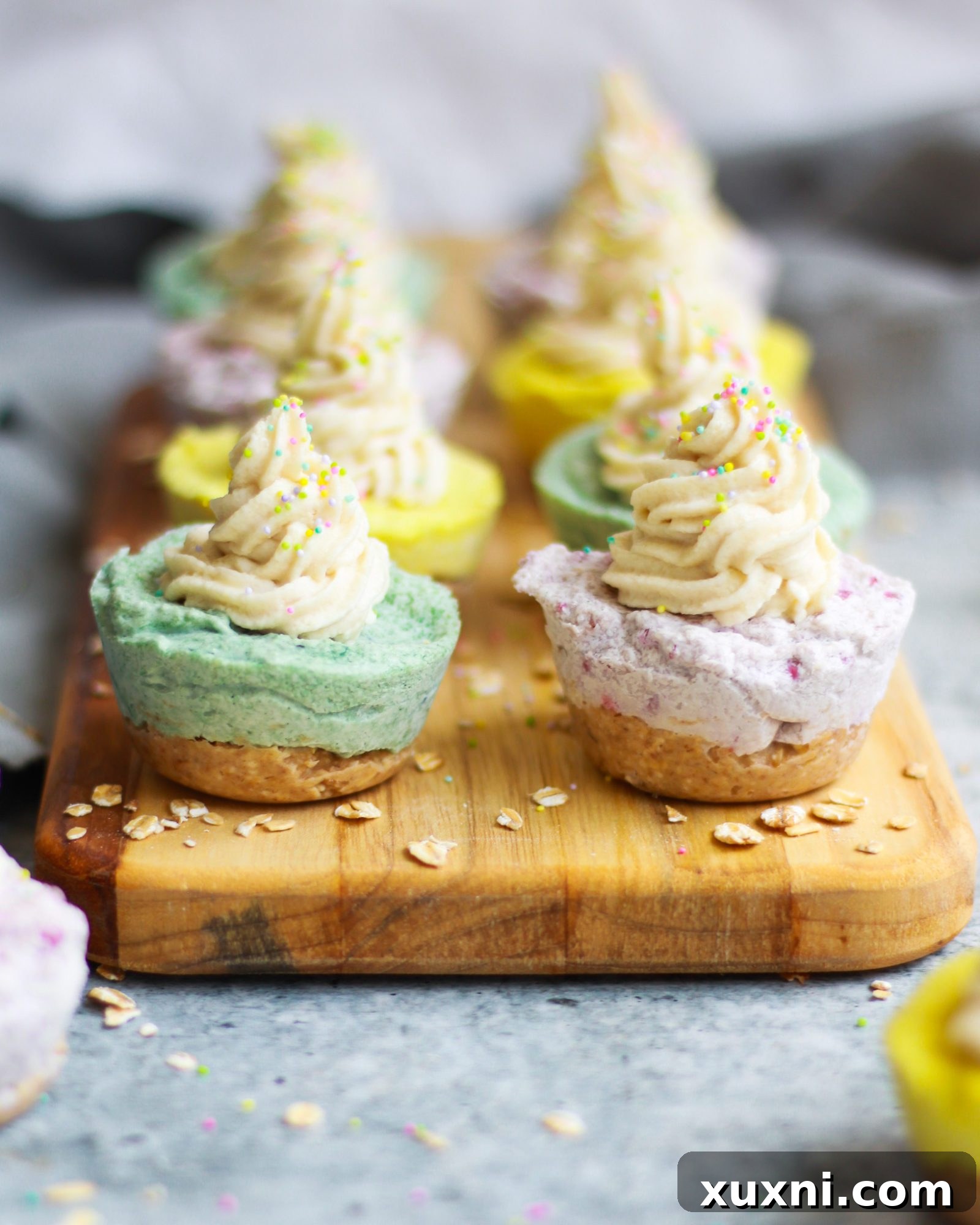 A wooden board showcasing a variety of naturally colored mini vegan cheesecakes.