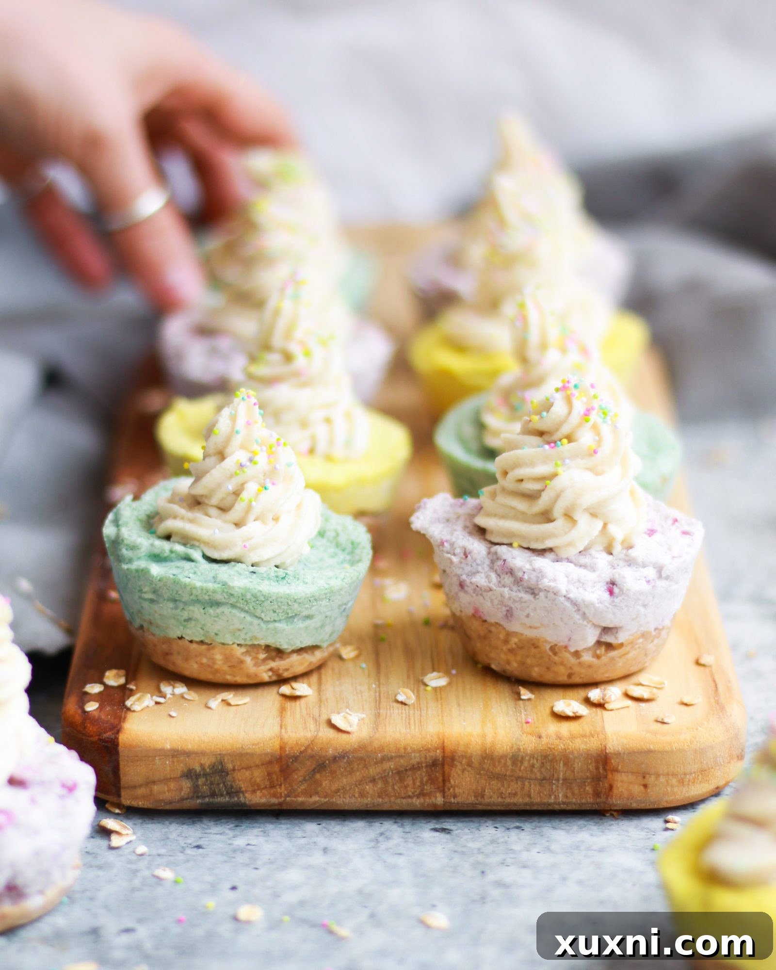 A beautifully frosted mini vegan cheesecake on a wooden board, with a hand reaching for it.