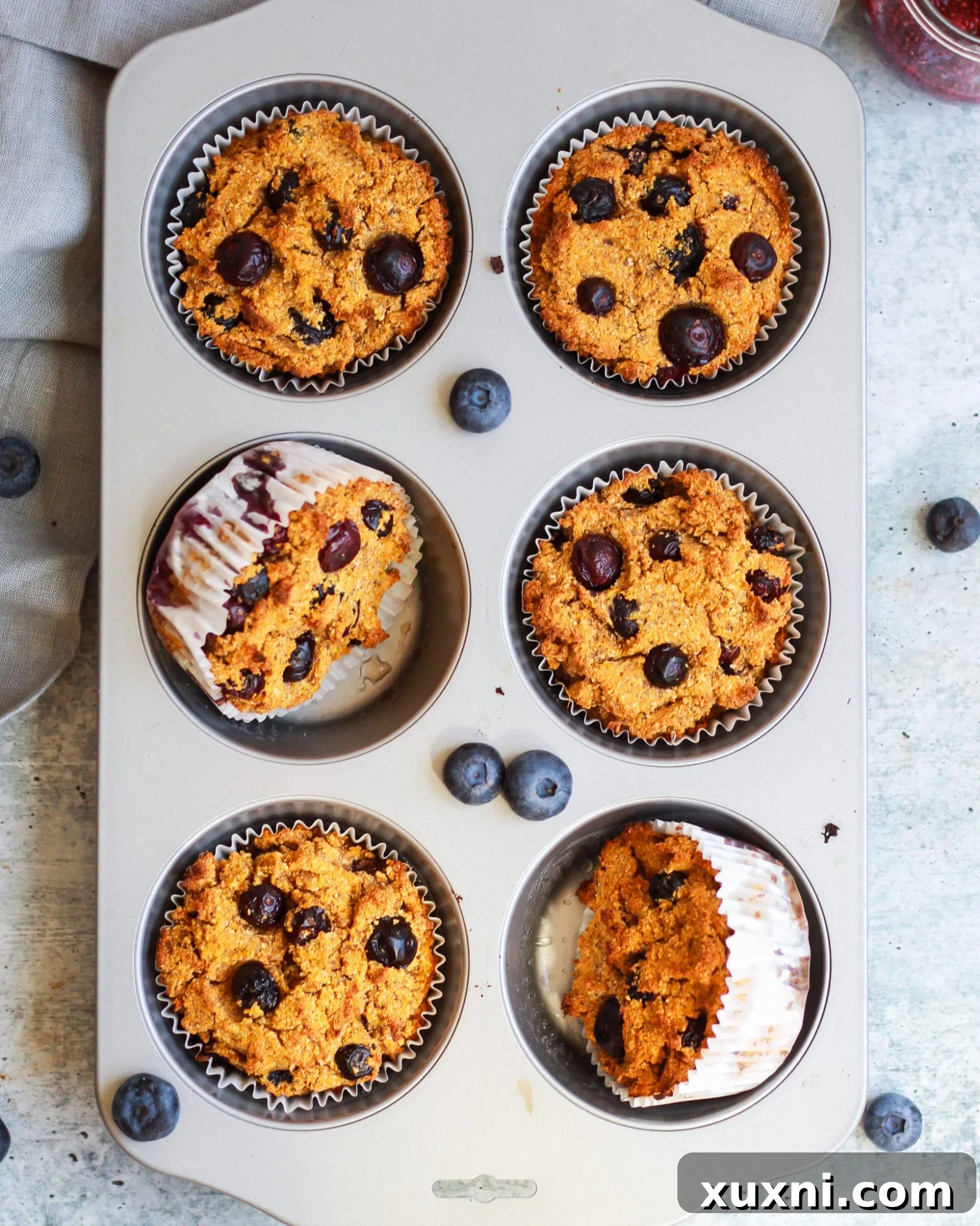 A muffin tin filled with freshly baked vegan paleo blueberry muffins, with a few turned over to show their soft underside.