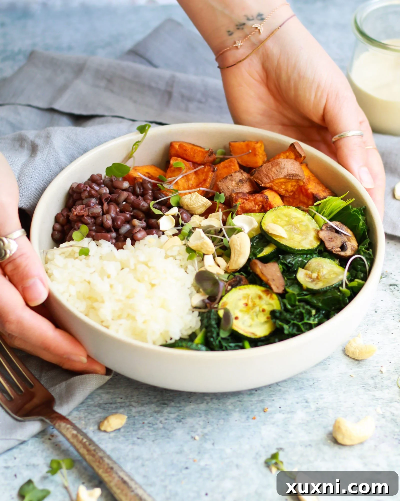 3/4 shot of macrobiotic bowl held by hands with vegan tahini sauce