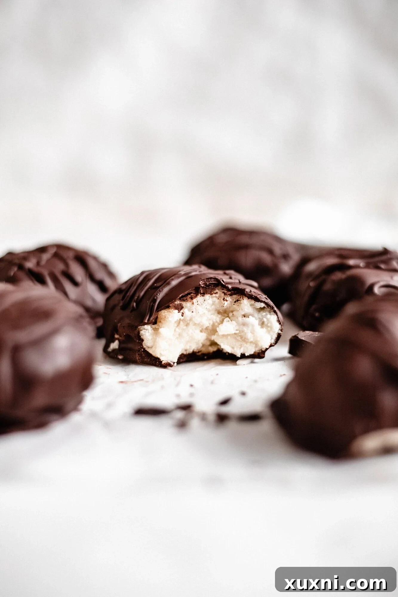 A delightful Paleo coconut cream egg with a bite taken out, showcasing the smooth, rich chocolate shell and the soft, white coconut filling within.