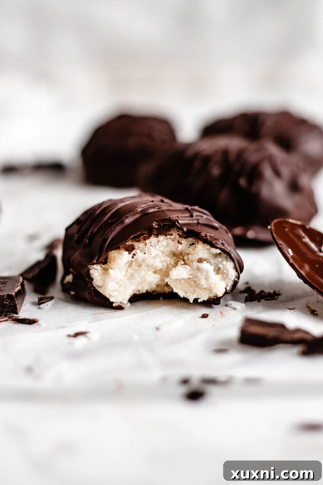 A close-up of a Paleo vegan coconut cream egg with a bite taken out, revealing the creamy white coconut filling contrasting with the dark chocolate shell.