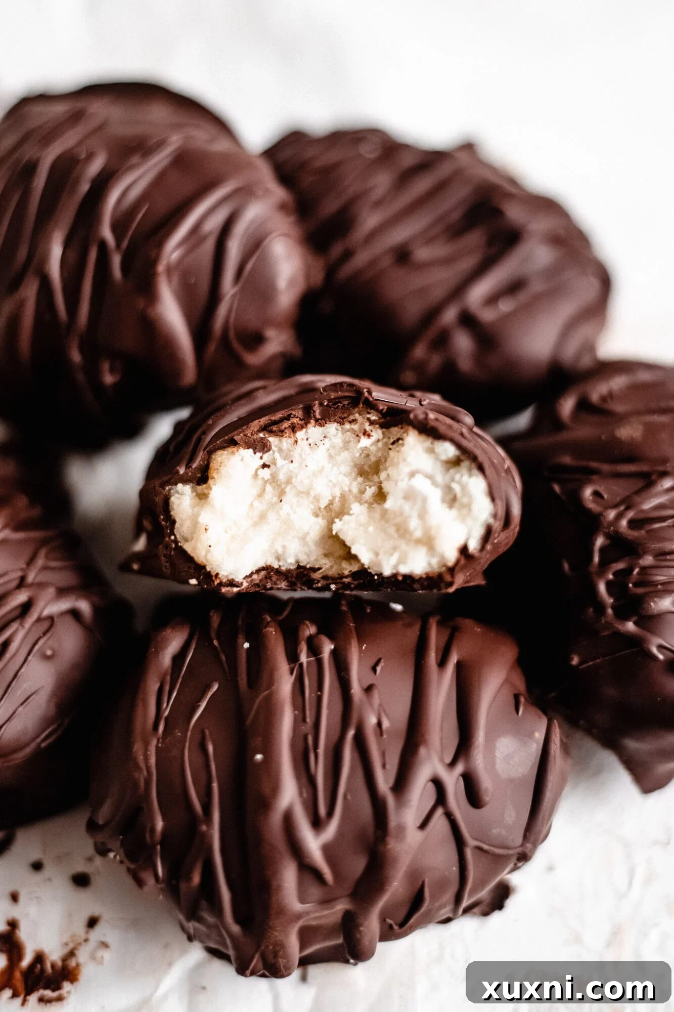 A single Paleo vegan coconut cream egg, half-eaten, highlighting its rich dark chocolate exterior and the moist, fluffy coconut filling within.