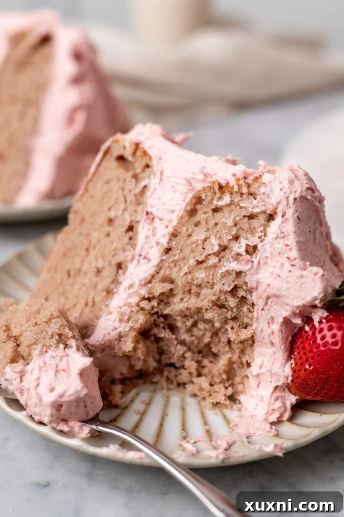 Close-up of a slice of vegan strawberry cake on a plate with a fork, showing the fluffy texture.