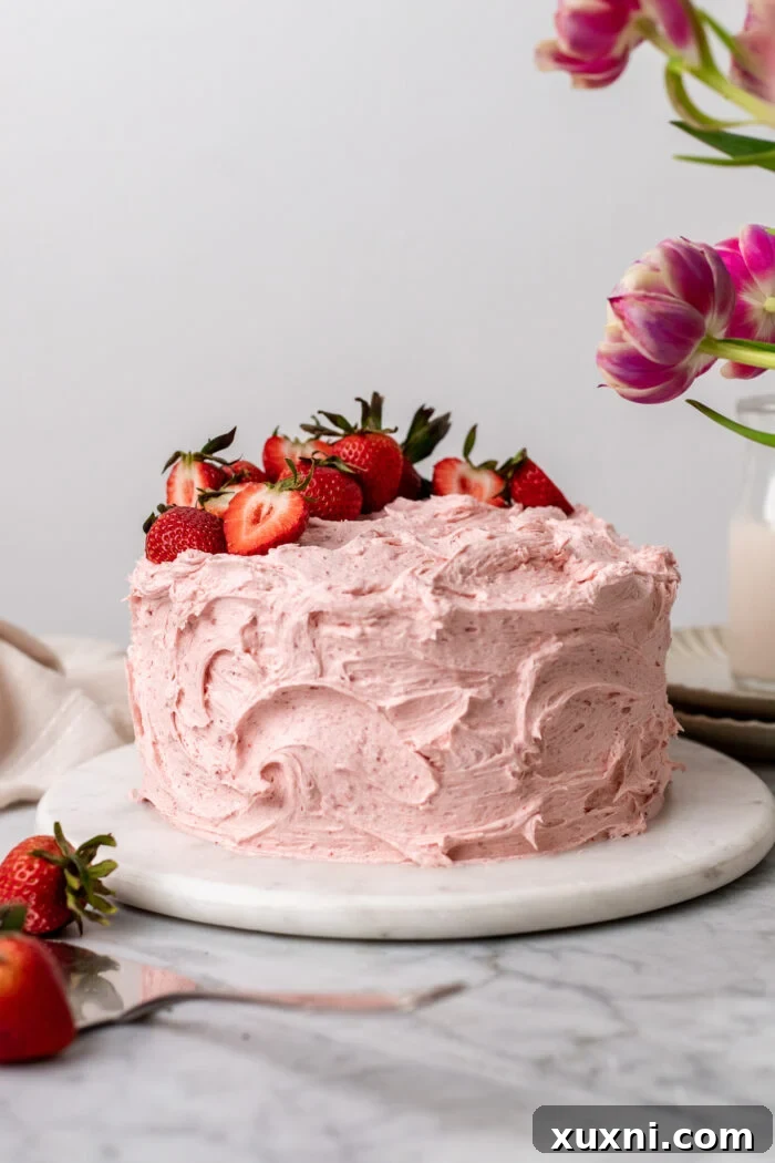 A beautifully frosted vegan strawberry cake adorned with fresh strawberries.