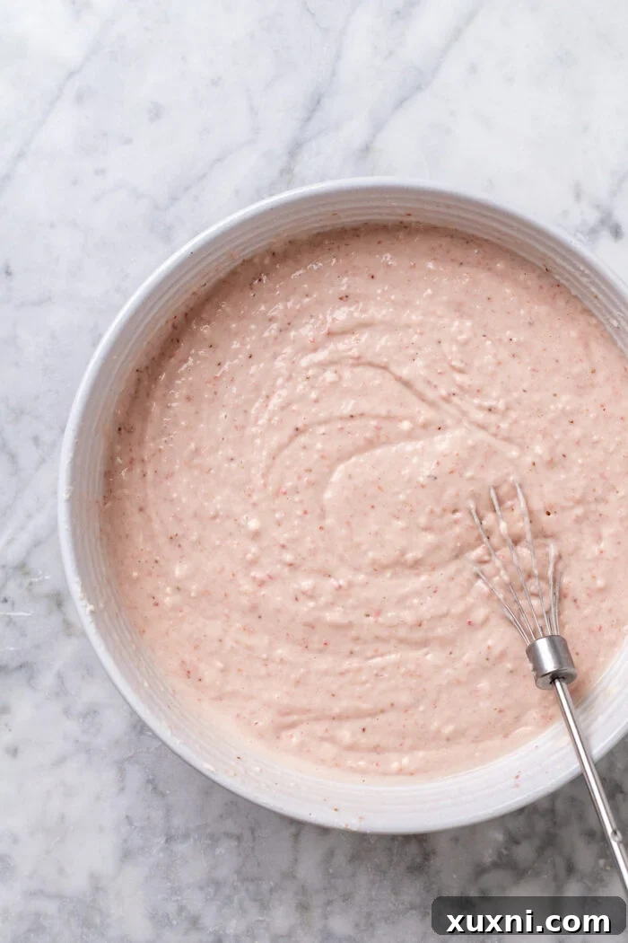 Mixing strawberry cake batter with dry ingredients, revealing a thick, creamy texture.