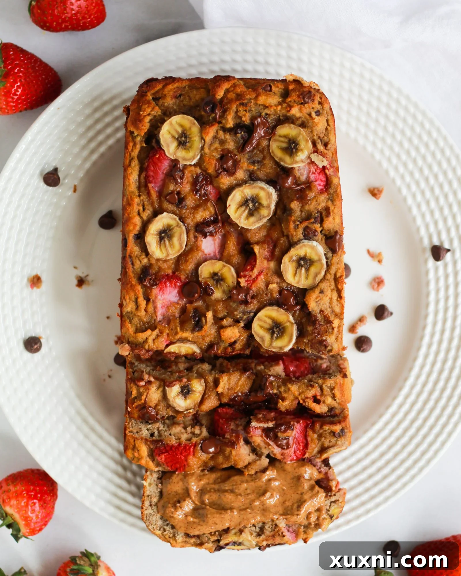 Sliced strawberry banana bread with chocolate chips and fresh strawberries on a white plate, showcasing its moist texture.