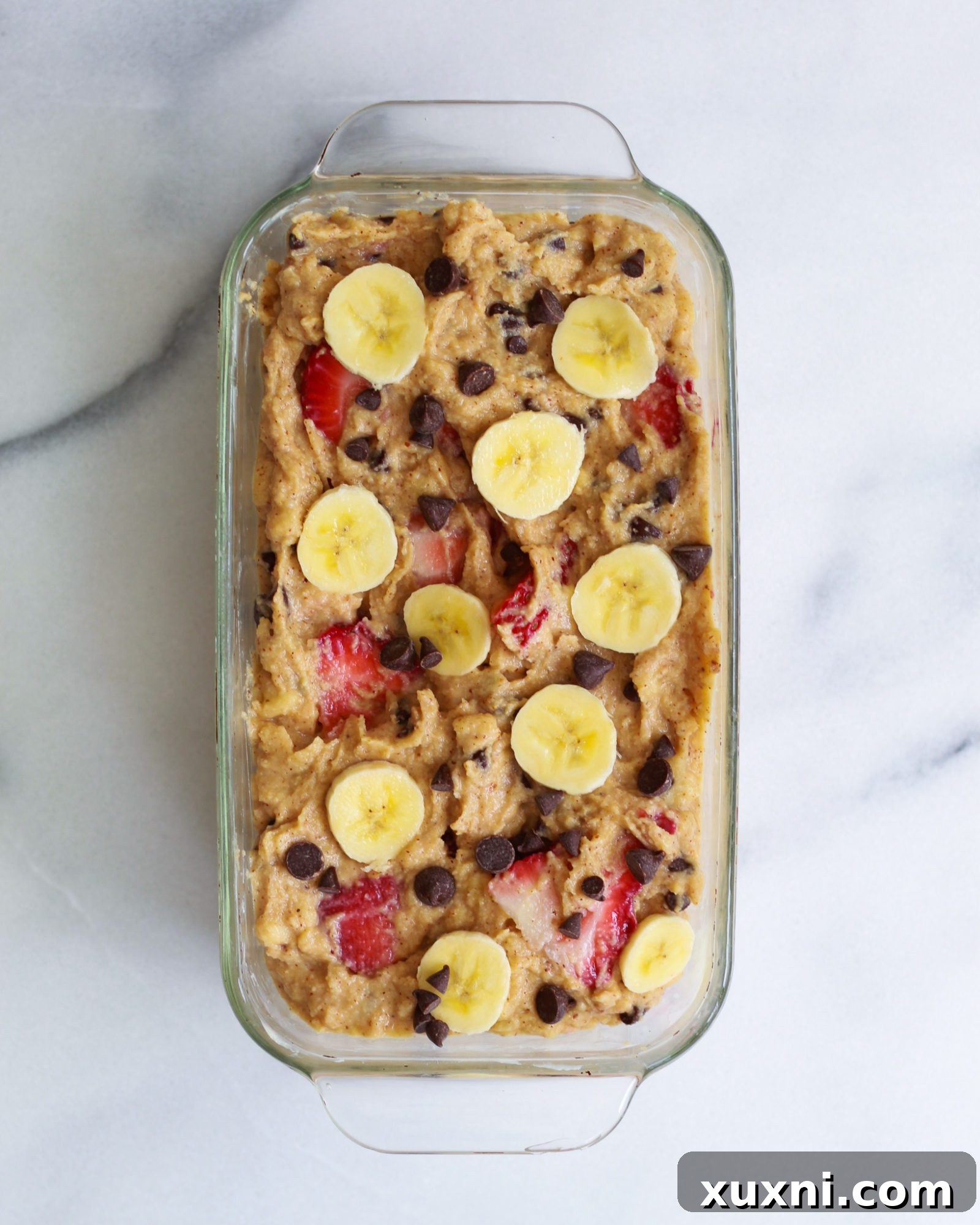 A vibrant, unbaked strawberry banana bread batter in a bowl, showcasing the fresh strawberries and chocolate chips.