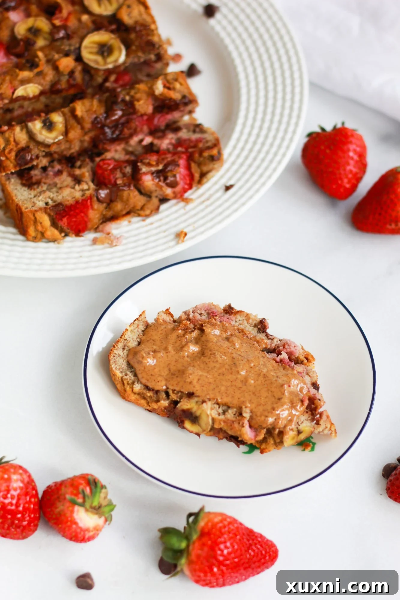 A delectable slice of strawberry banana bread, adorned with a smooth smear of almond butter, resting on a clean plate.