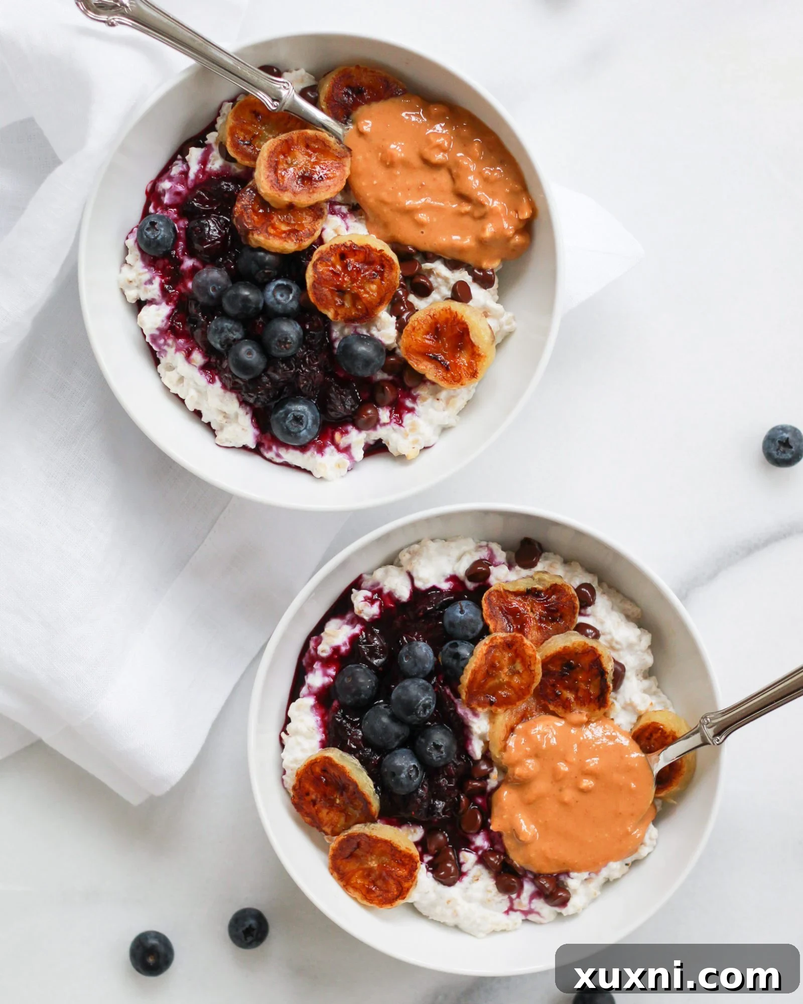 Two bowls of creamy oatmeal topped with banana, blueberries, and peanut butter