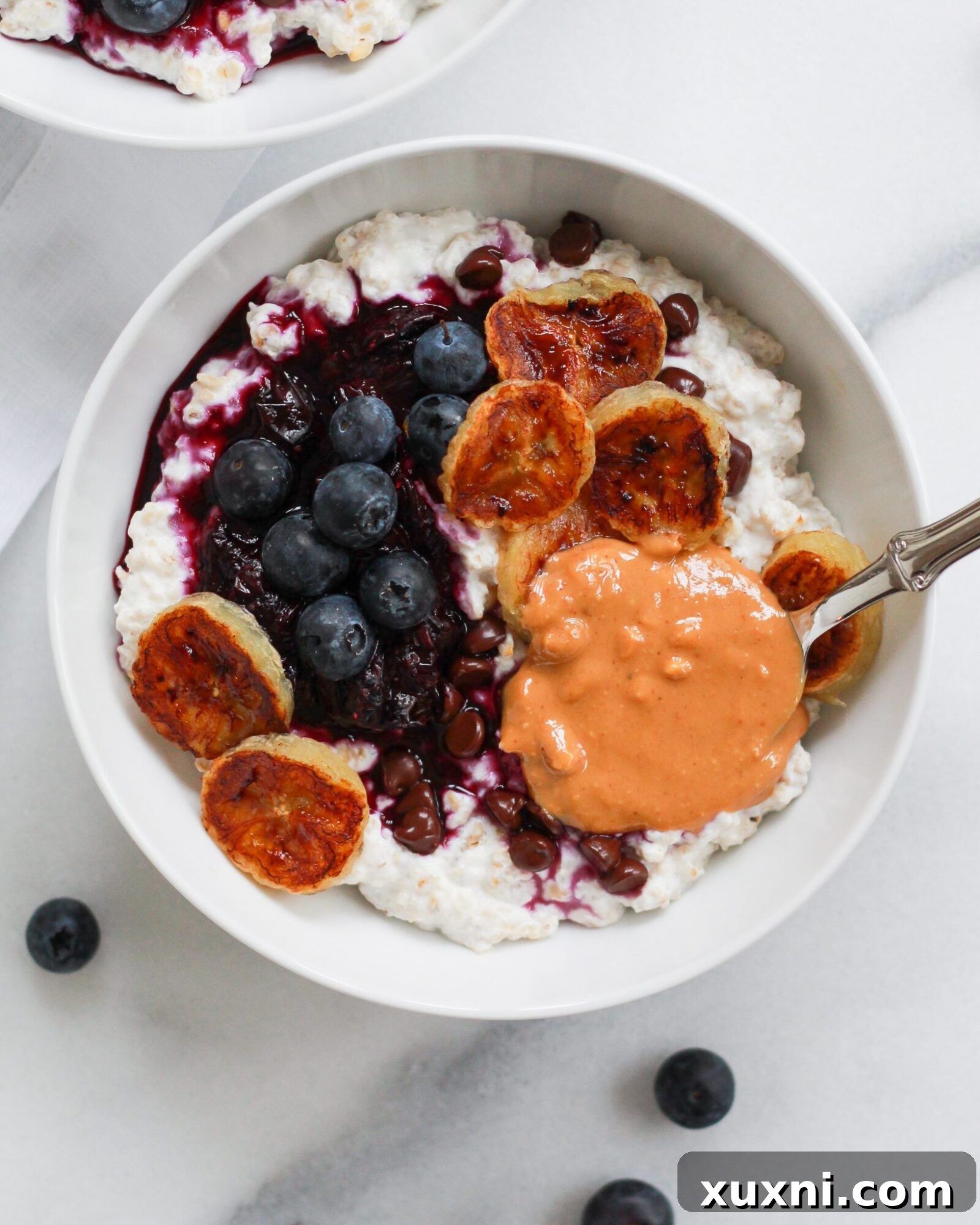 Creamy bowl of oatmeal with a dollop of peanut butter on white marble surface