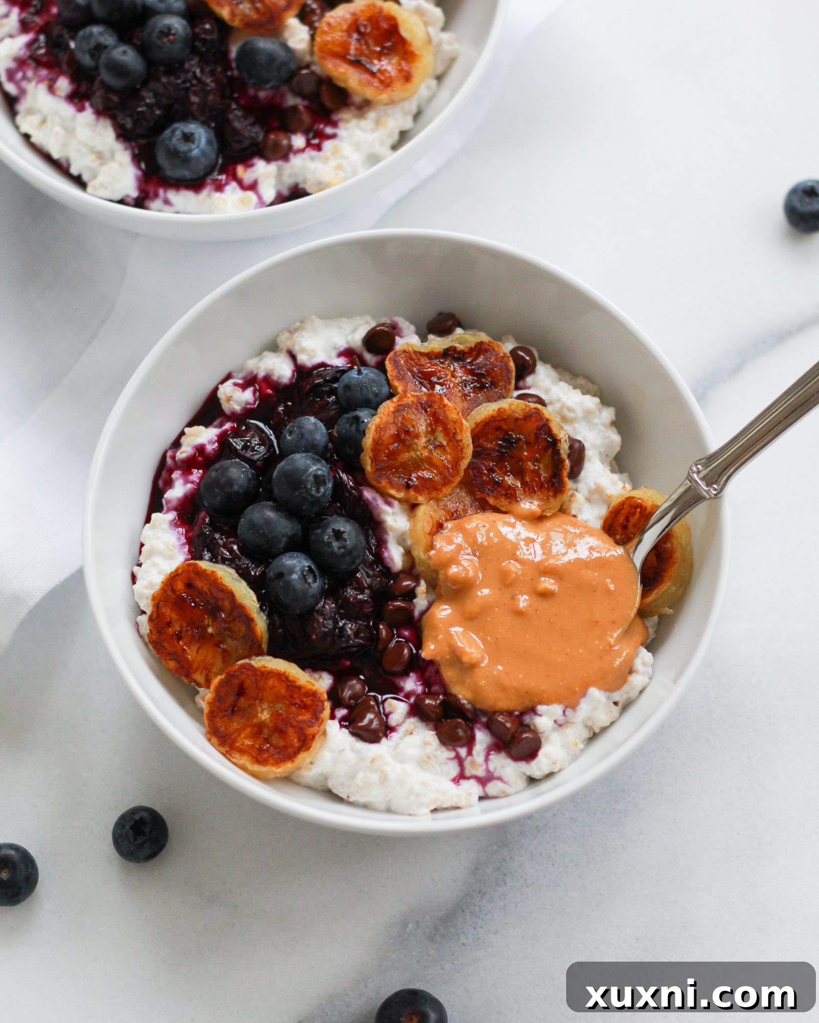 Bowl of oatmeal with a spoon resting in peanut butter on white marble