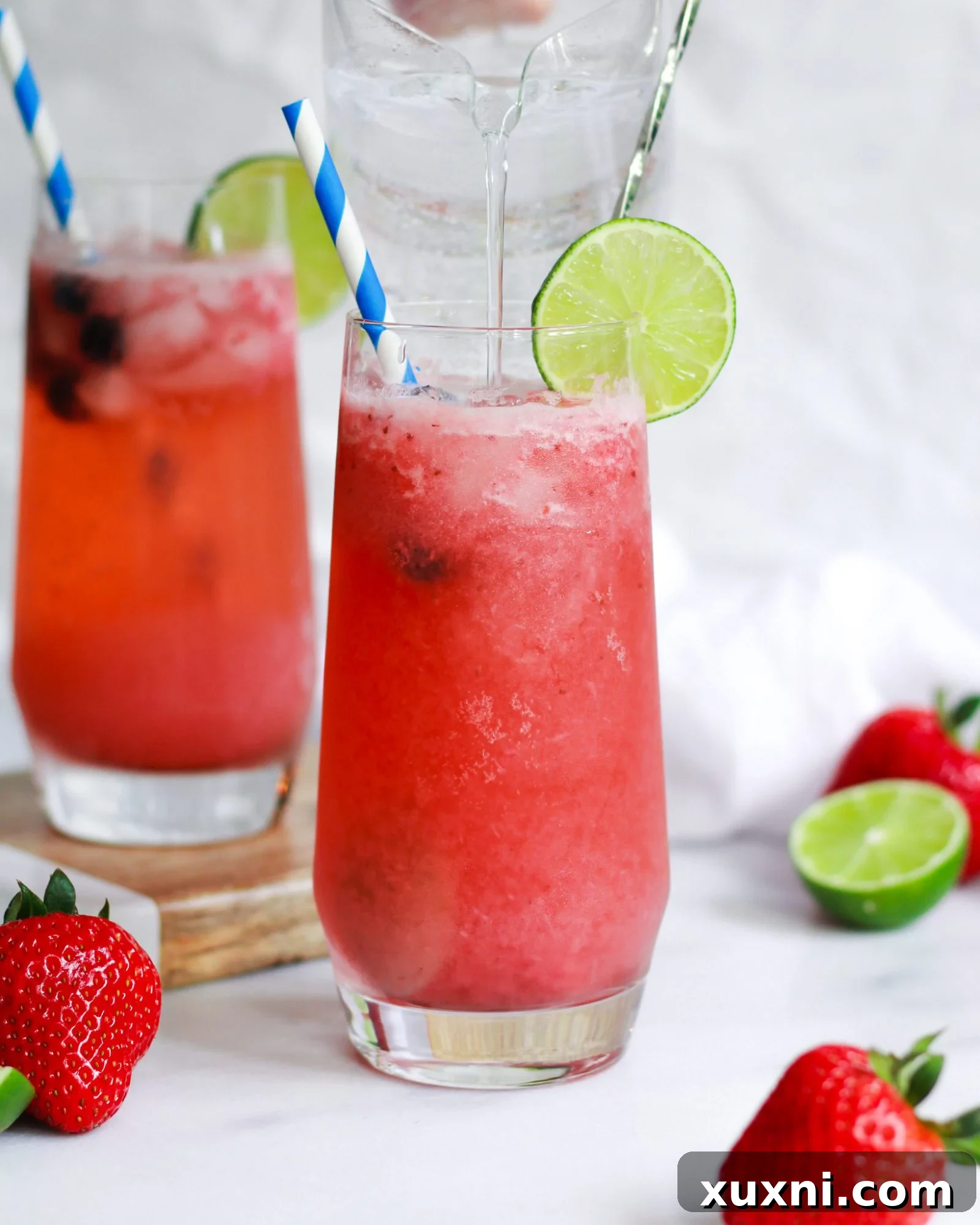Blushing Berry Mockarita 8 A hand pouring seltzer water into a glass filled with strawberry puree and ice, creating a fizzy mocktail.