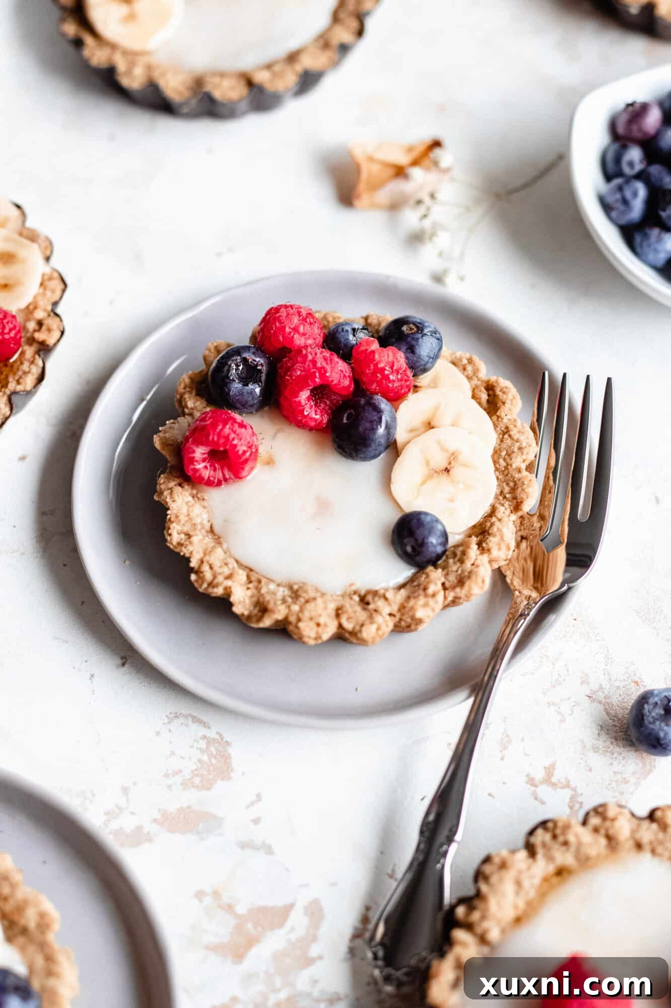 A mini fruit tart on a plate with a bite taken, revealing the creamy custard and berry layers, appealing to tastebuds.