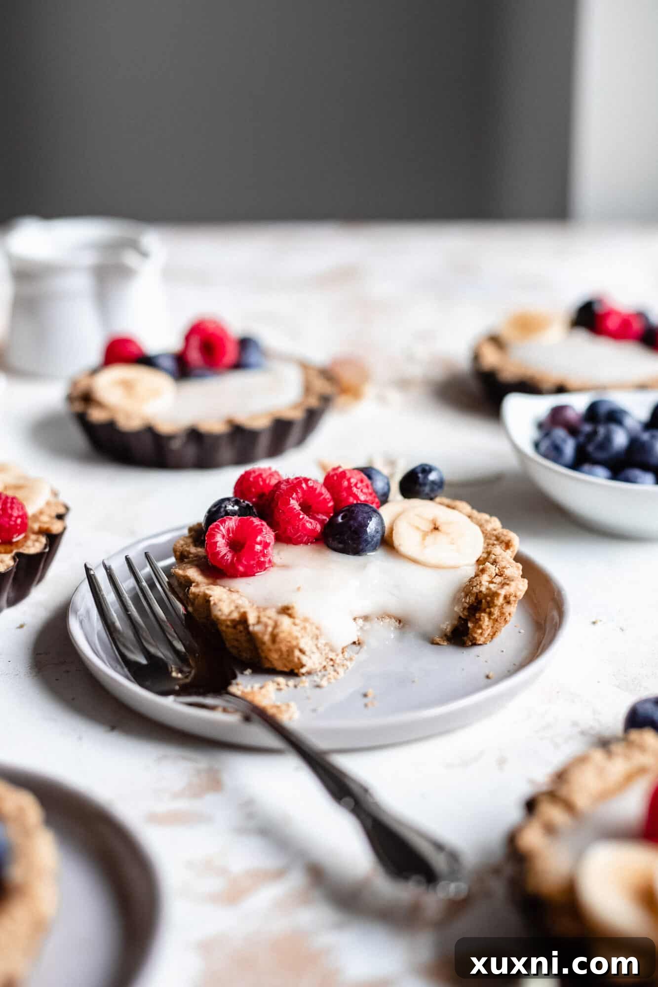Another view of a mini fruit tart on a plate with a bite taken, emphasizing its fresh ingredients and inviting texture.