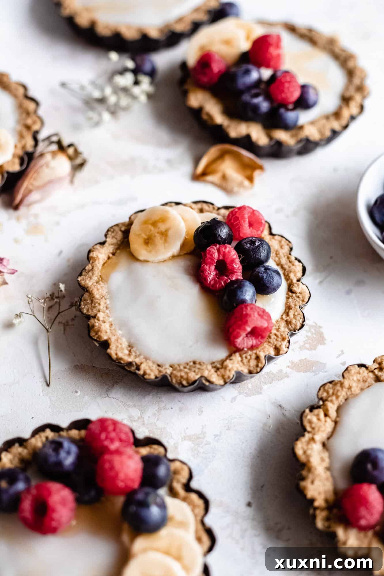 Close-up of healthy vegan mini fruit tarts topped with a generous assortment of fresh berries, ready to be served.