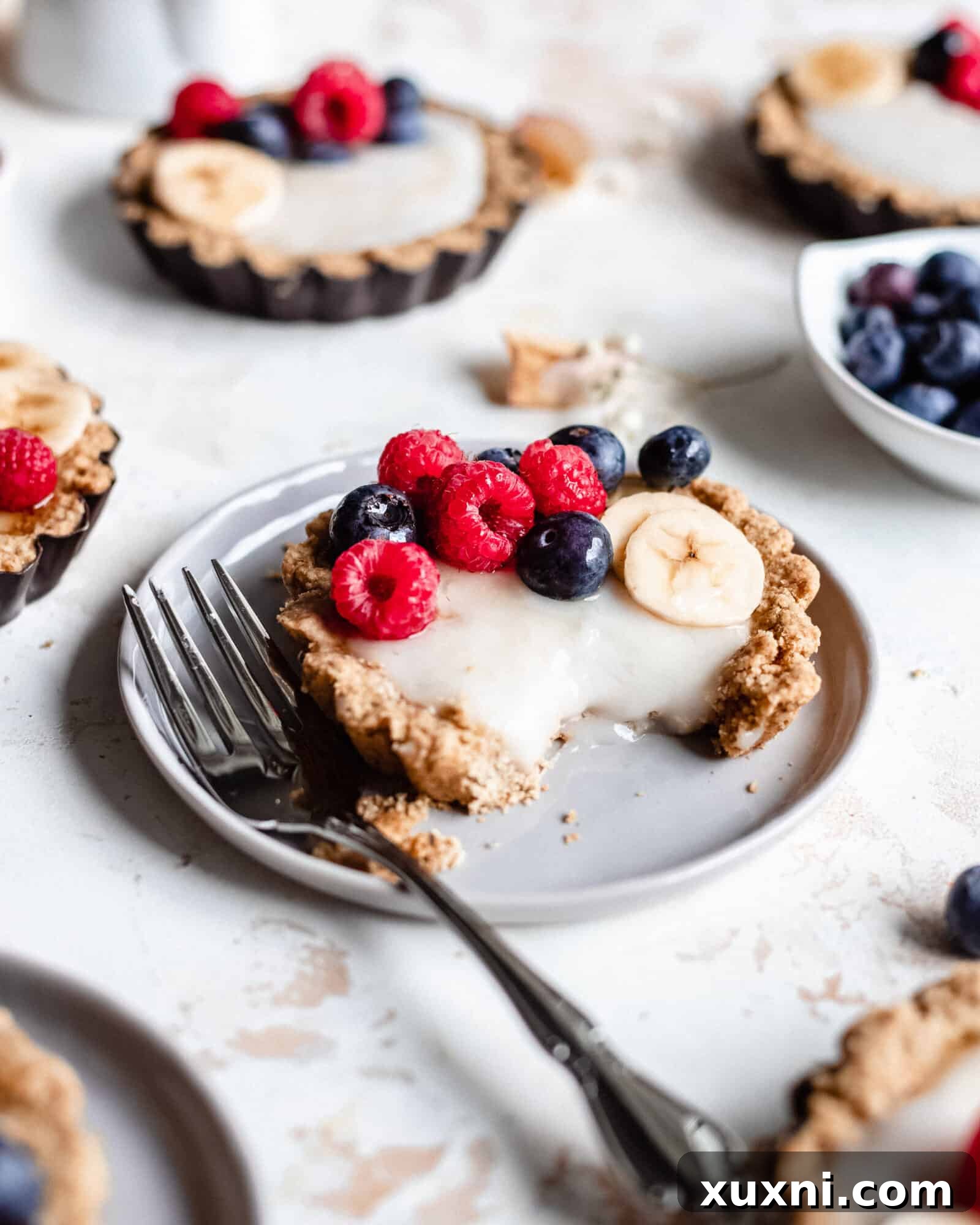A single vegan mini fruit tart with vanilla custard and fresh berries, a bite taken out, showcasing its delicious layers.