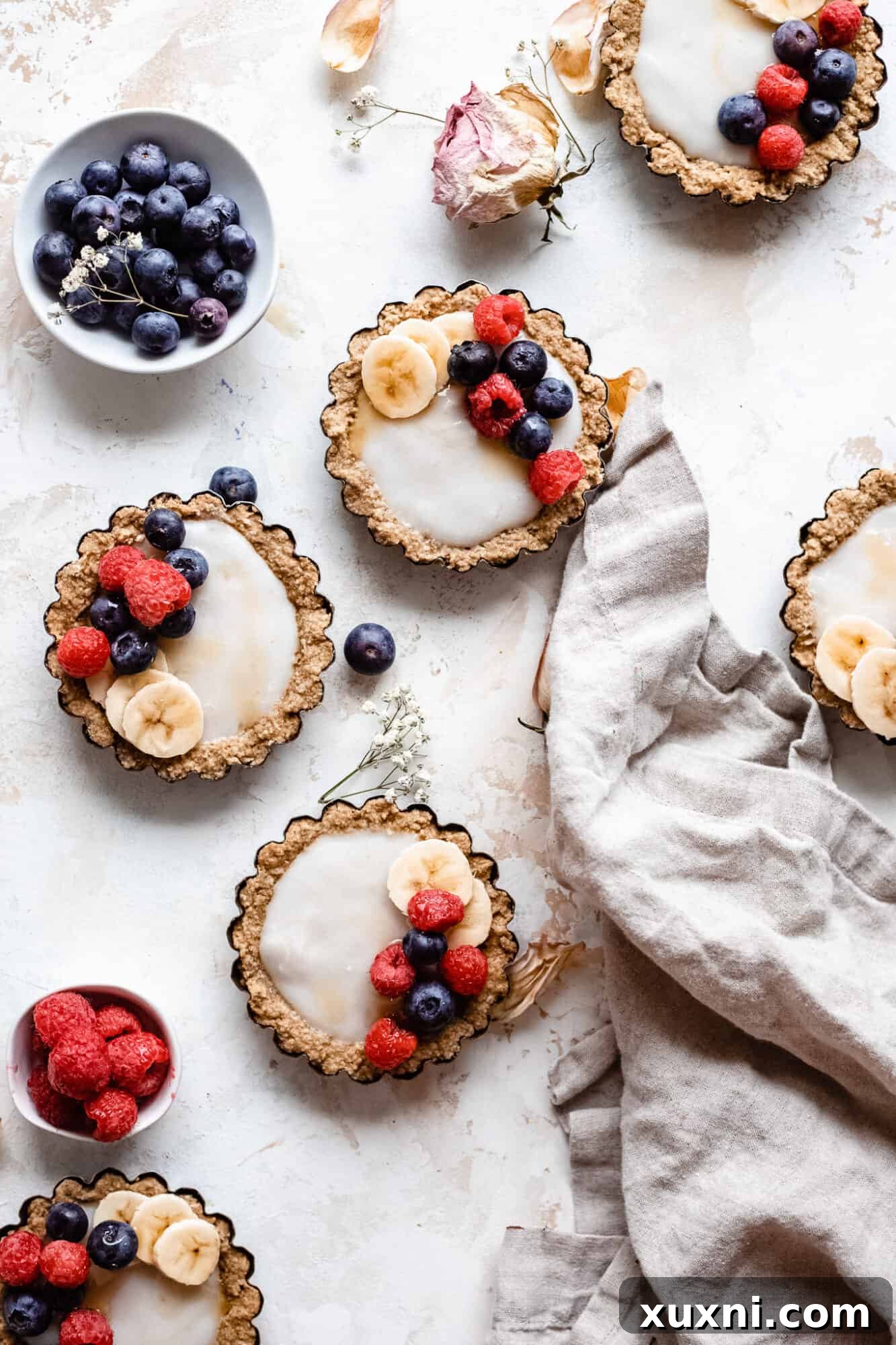 Arrangement of healthy vegan mini fruit tarts with vanilla custard and fresh berries, on a patterned cloth, ready for serving.