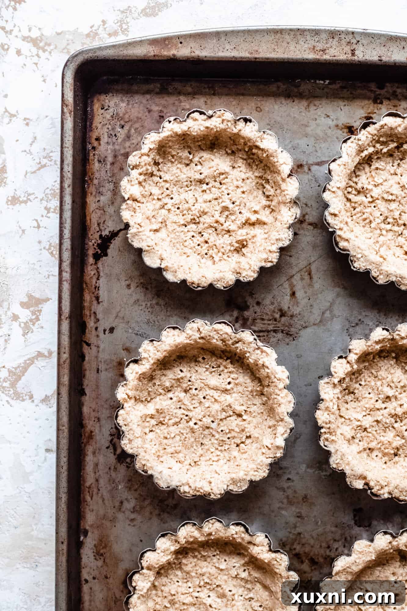 Unbaked vegan oat crust dough pressed into mini tartlet cups, ready for the oven.