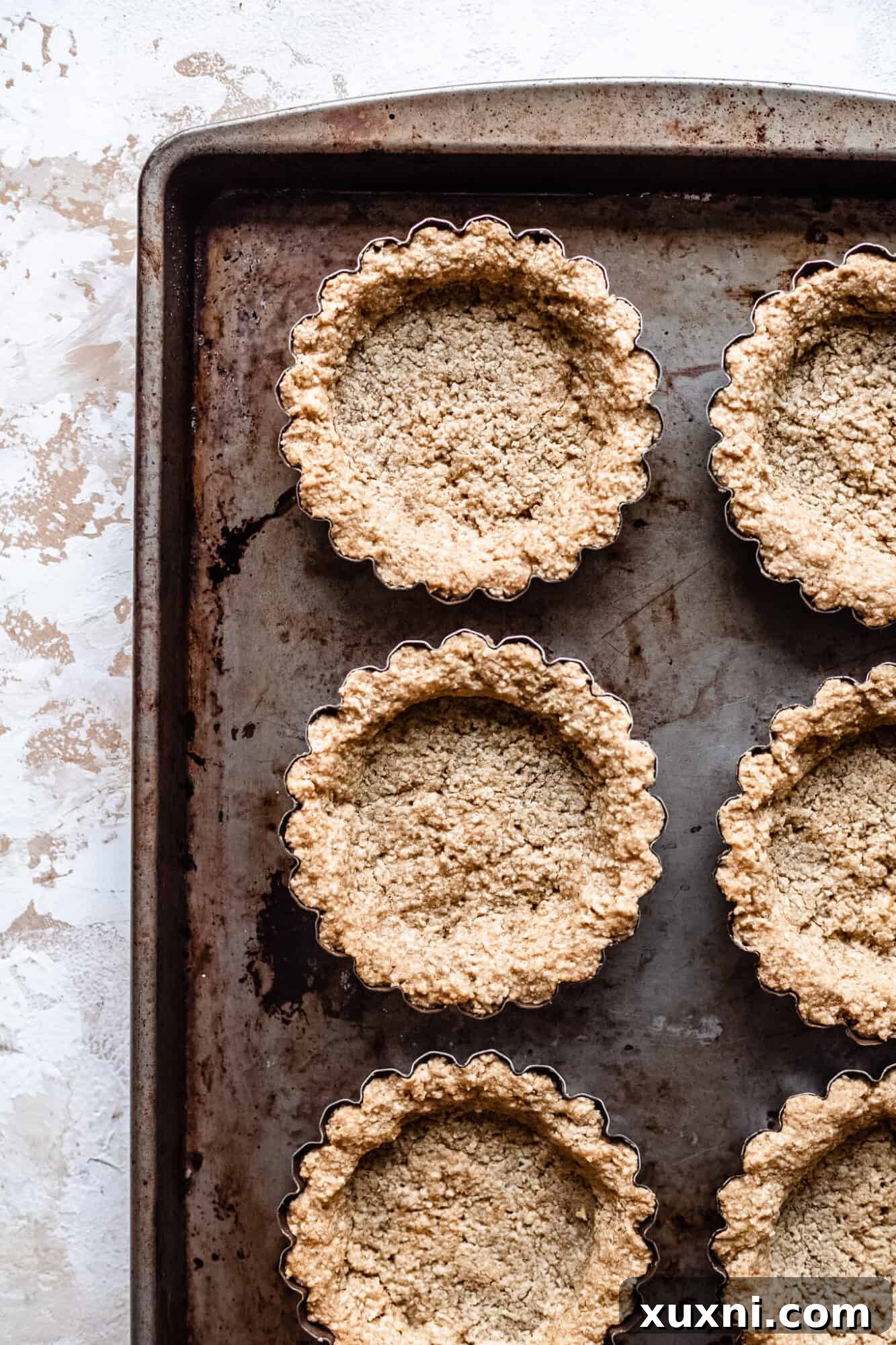 Golden brown baked vegan oat crust tartlets, cooled and ready for the custard filling.