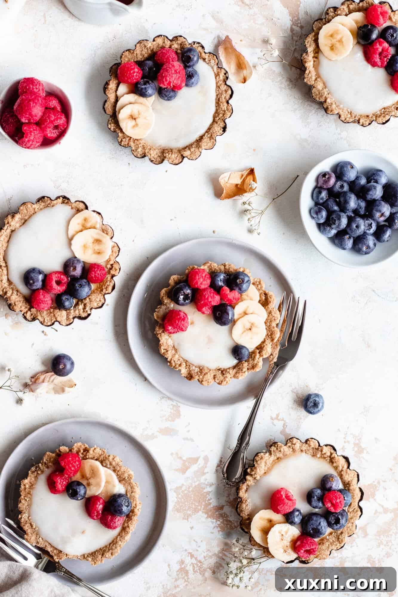 Two gluten-free fruit tarts on individual plates, garnished with berries, ready to be enjoyed.