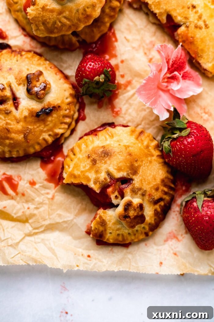 A partially eaten vegan strawberry hand pie, revealing its delicious filling, with fresh strawberries artfully placed nearby on a wooden surface.