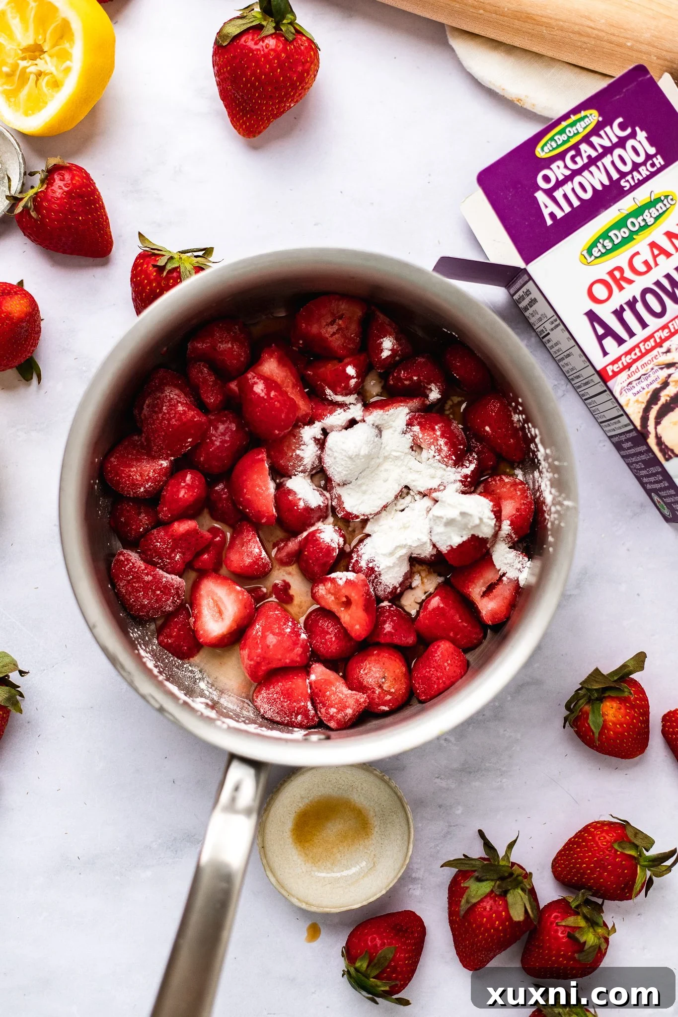 Raw ingredients for vegan strawberry pie filling, including sliced strawberries, lemon, starch, and vanilla extract, ready to be cooked in a saucepan.