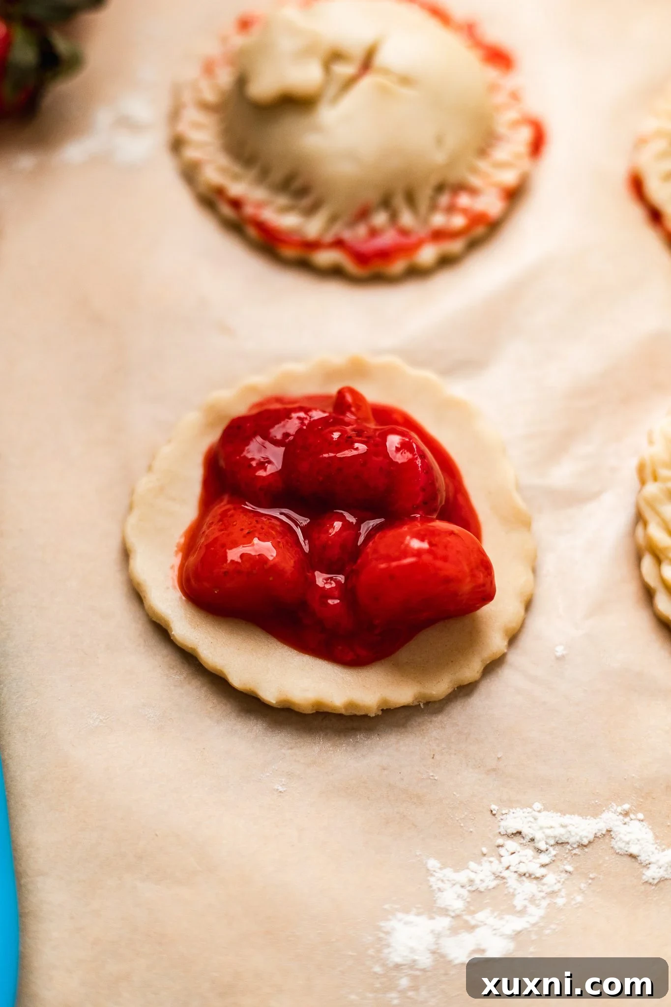 A single round of pie crust placed on parchment paper, topped with a generous spoonful of strawberry pie filling in the center.