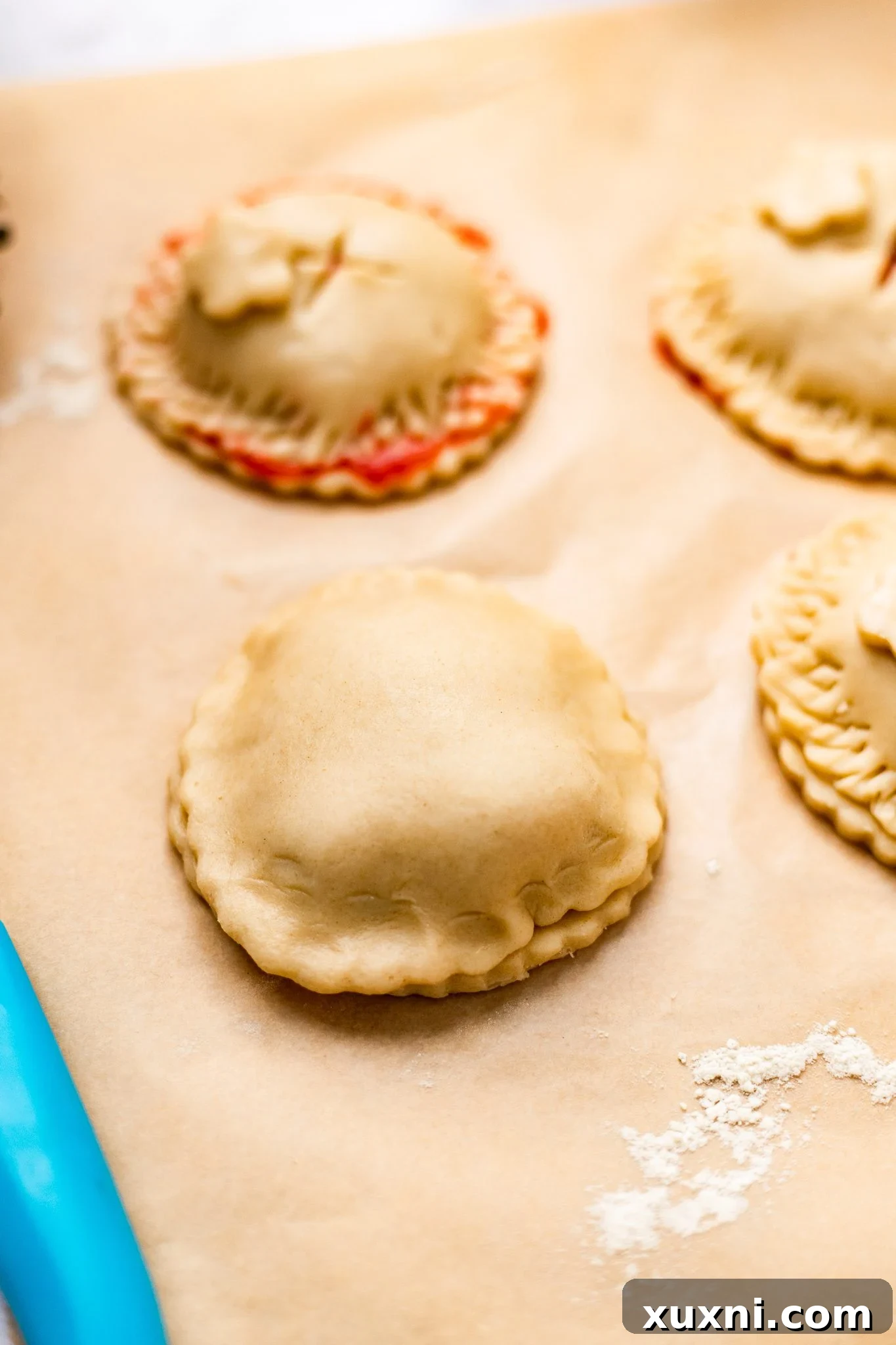 A fully assembled, sealed vegan strawberry hand pie on parchment paper, with a second crust placed on top of the filling and crimped edges.