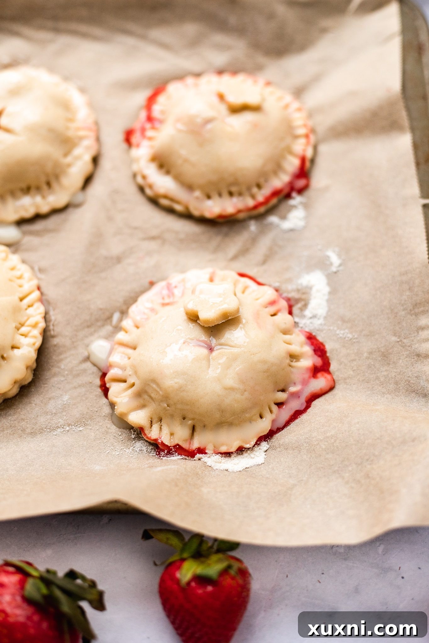 Unbaked vegan strawberry hand pies on a baking sheet, freshly brushed with a vegan egg wash, ready for the oven.