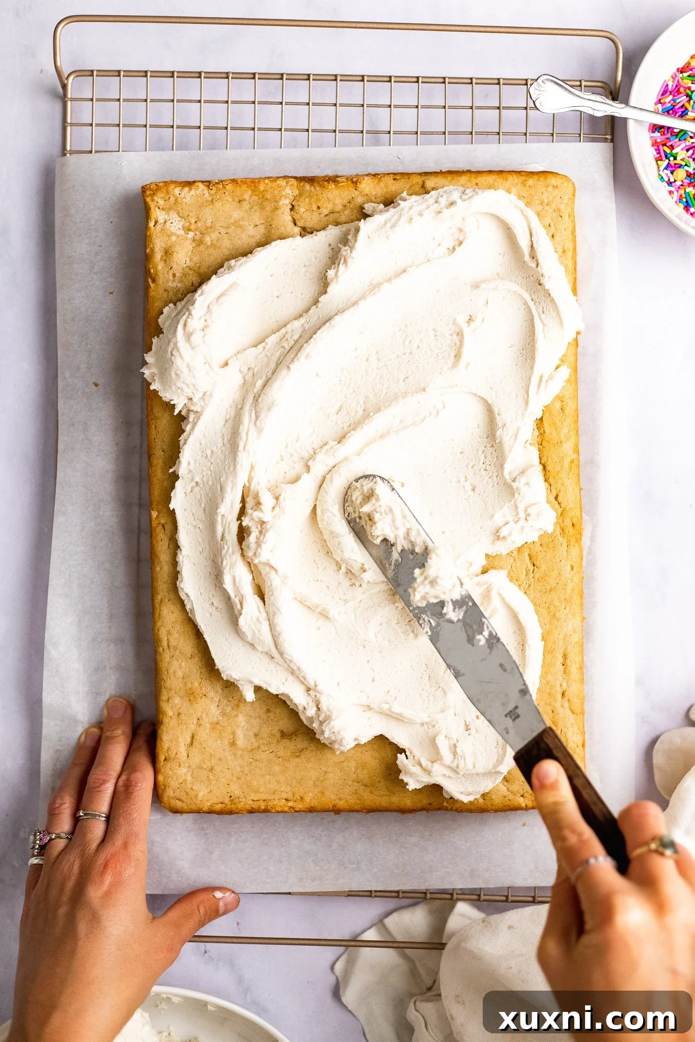 Easy & Delicious Vegan Vanilla Sheet Cake 10 applying frosting onto a vanilla sheet cake with an offset spatula