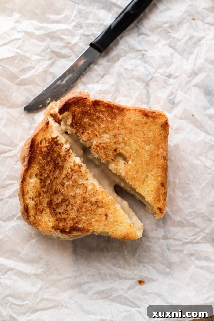 A perfectly golden-brown vegan grilled cheese sandwich, sliced in half and served on parchment paper
