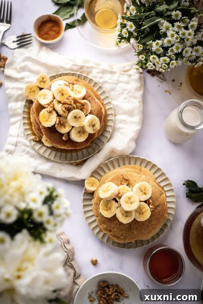 two plates of beautifully topped vegan banana pancakes with fresh fruit and syrup